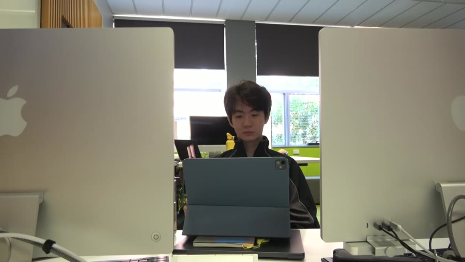 A seated performer framed by classroom computer monitors.